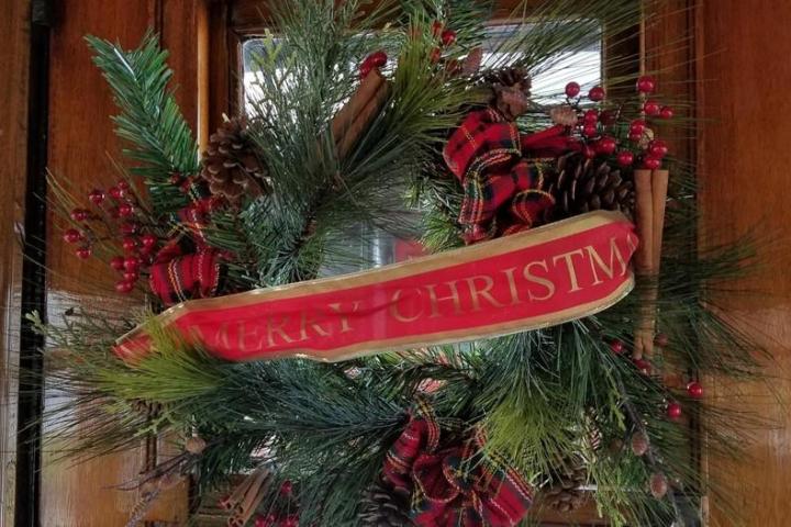 A Christmas wreath on a door with red ribbons, pinecones, and other festive decorations.