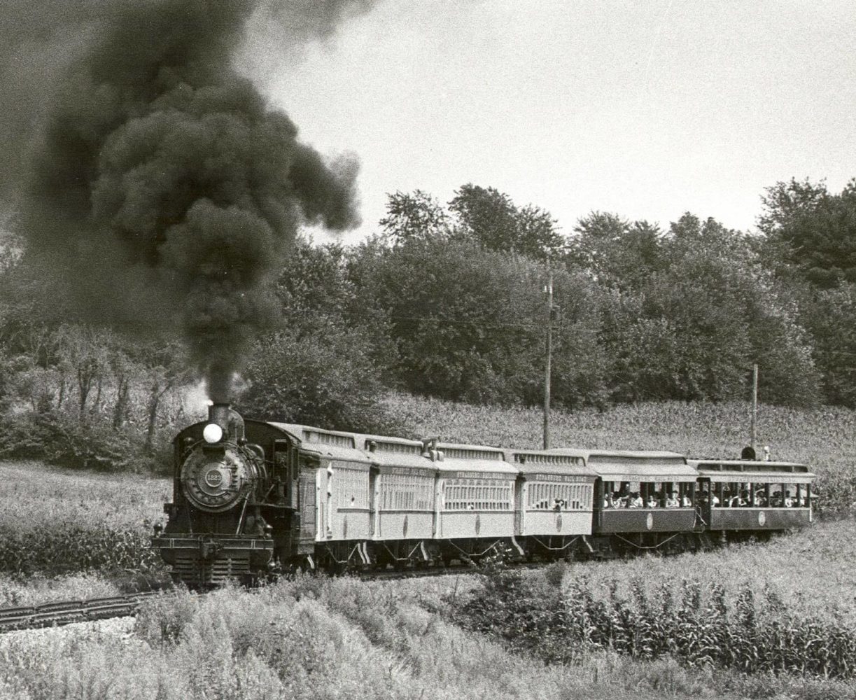 A steam engine train traveling down train tracks near a field.