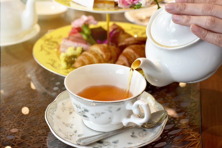 A teapot pouring tea into a flowered cup.